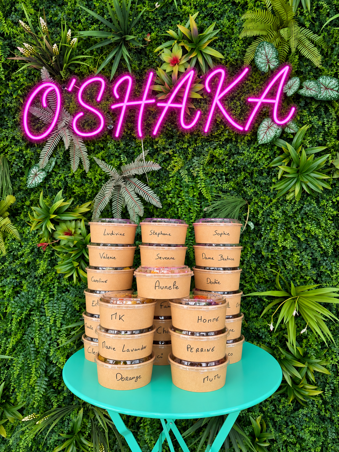 Commande groupée de pokebowls individuels devant le néon O’SHAKA et son mur végétal